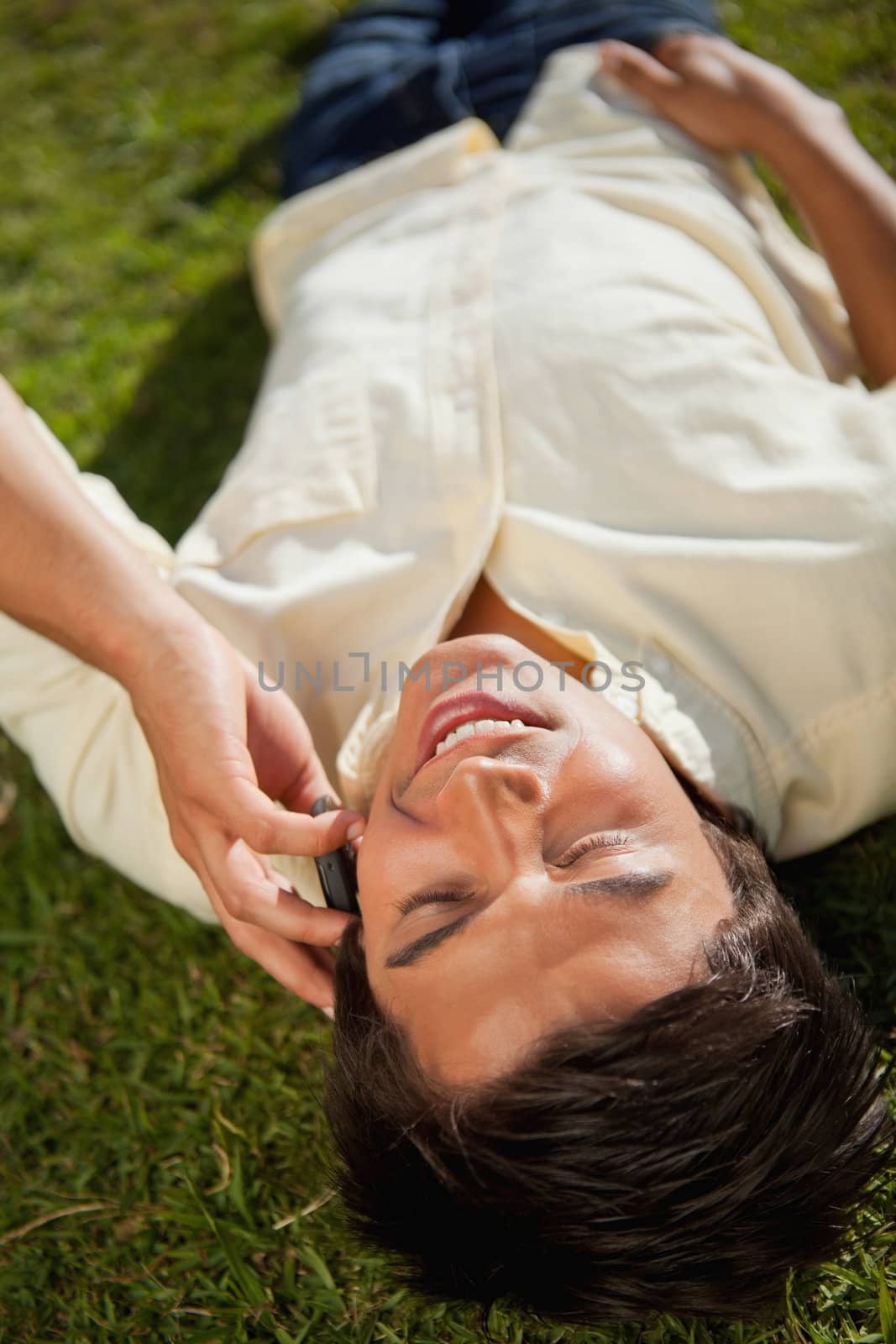 Close-up of a man with his eyes closed making a call over the phone as he lies down on the grass