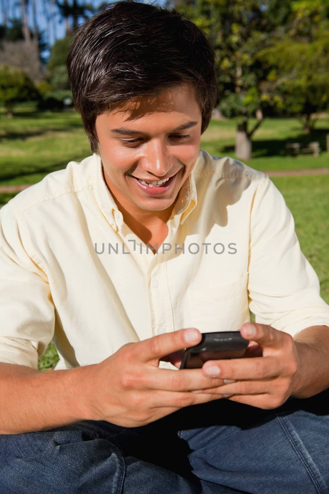 Man smiling as the uses a phone while he is sitting down on the grass