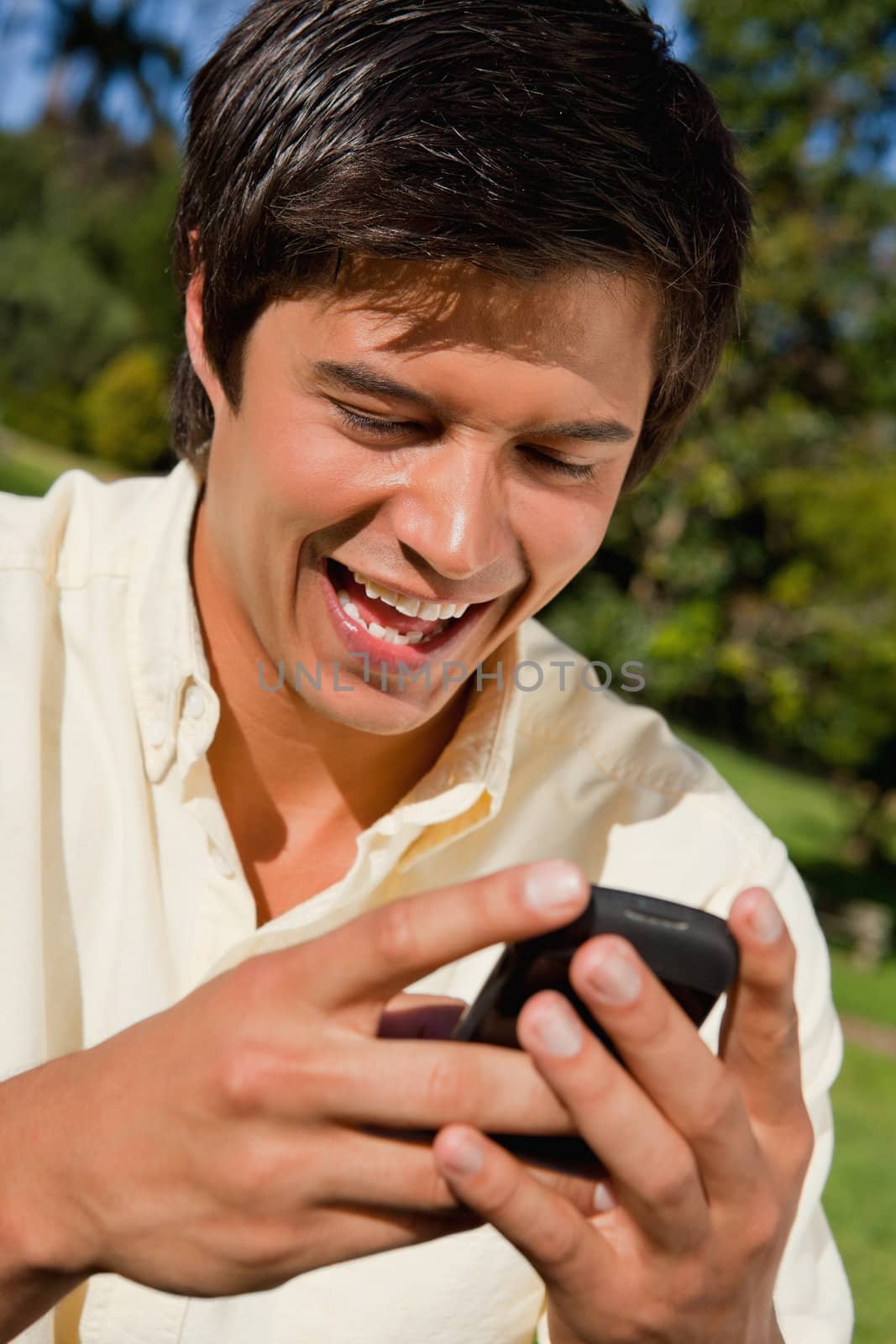 Close-up of a man smiling as the uses a phone while he is sitting down on the grass