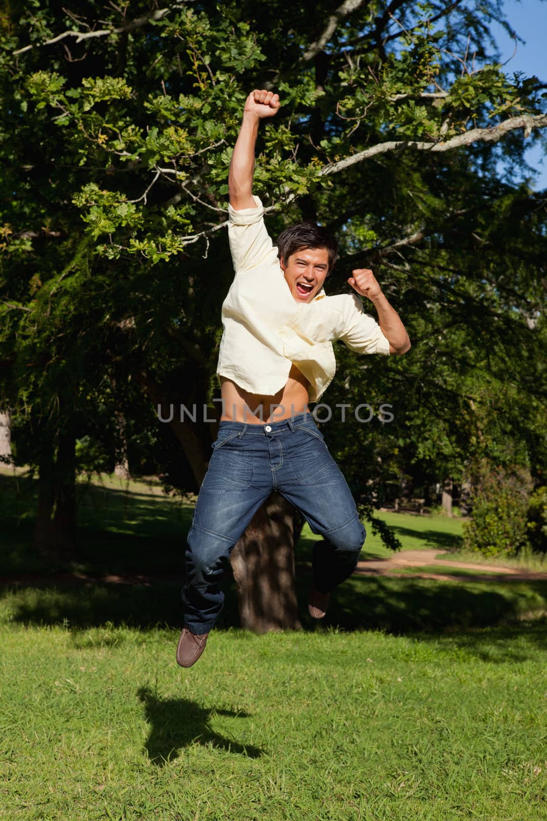 Man laughing as he jumps with his arms raised in celebration by Wavebreakmedia