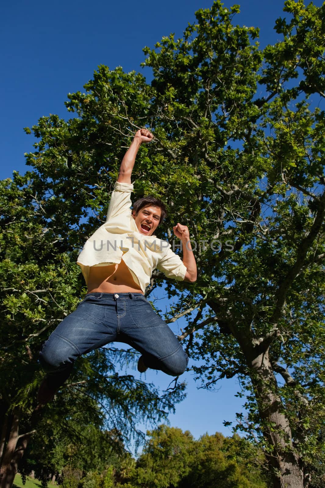 Man jumping off the ground while raising both his arms and his legs while he is celebrating in the park