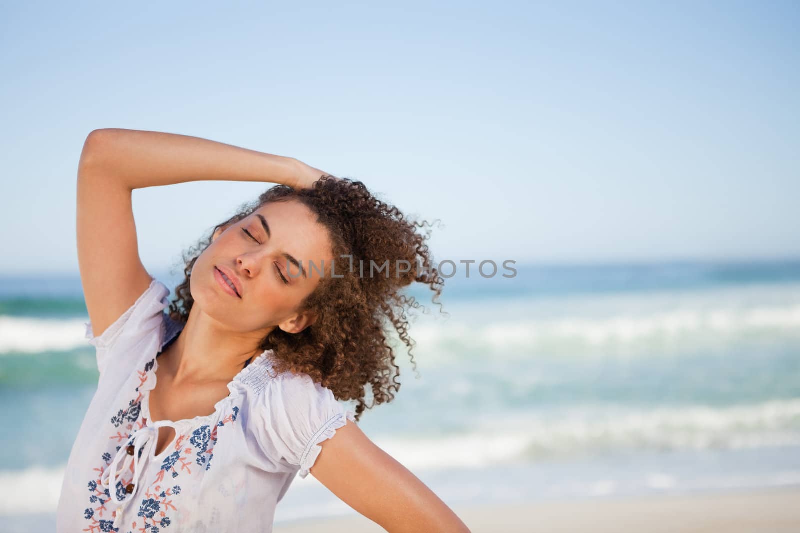 Young woman closing her eyes while holding her hair in front of the sea