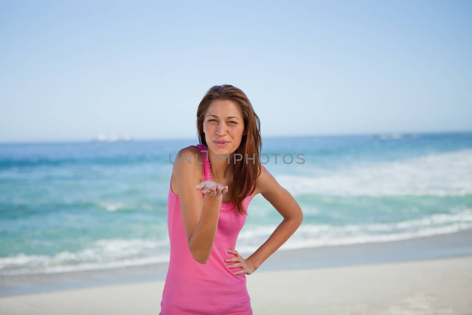 Young woman blowing an air kiss while standing in front of the sea