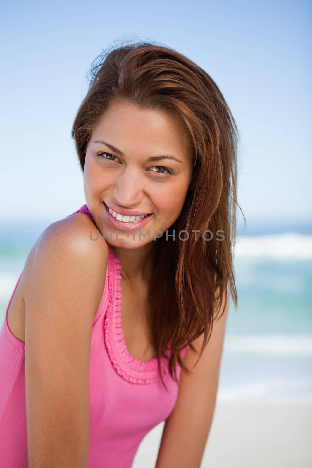 Young woman looking at the camera while standing in front of the sea and smiling