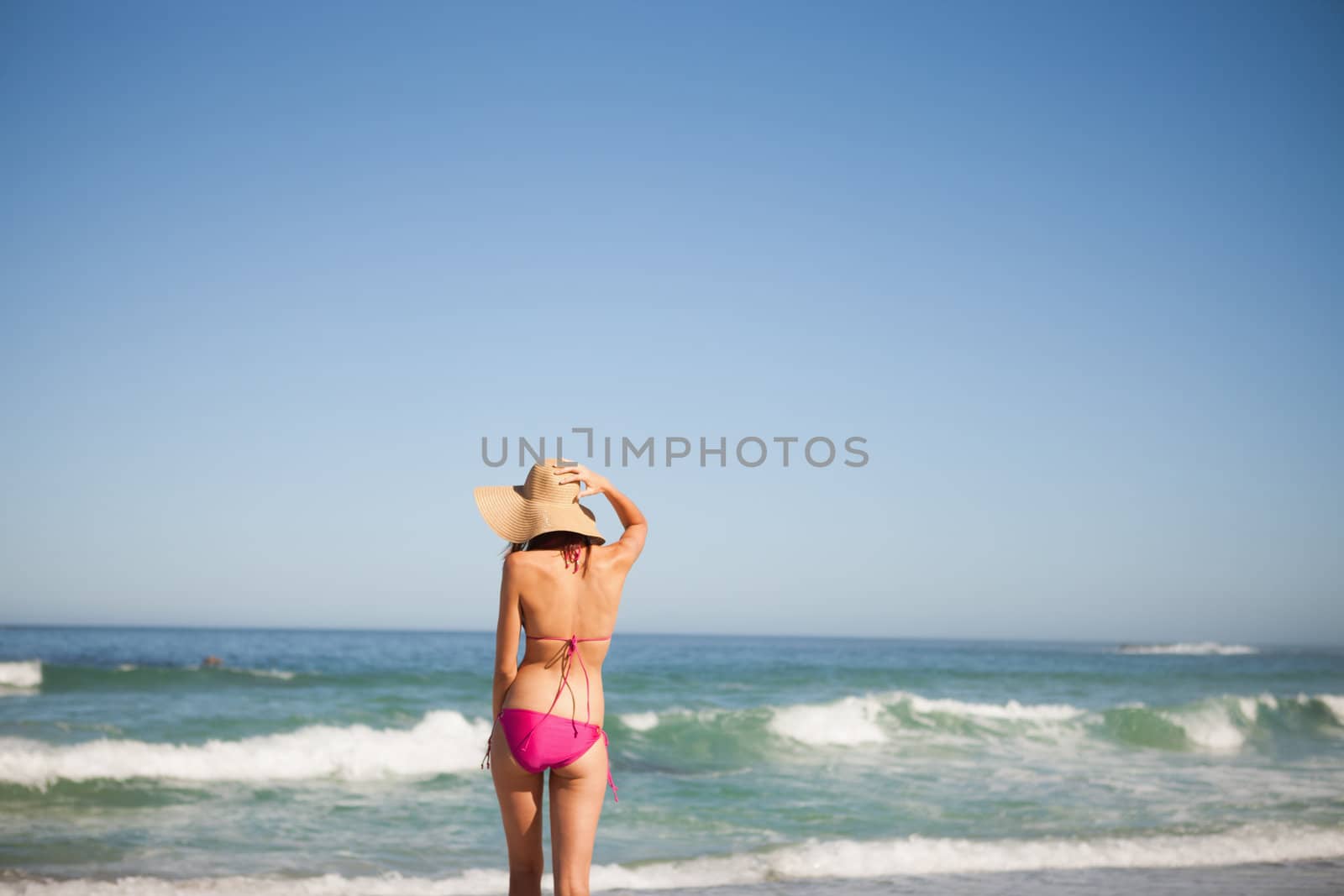 Back view of an attractive woman in beachwear standing on the beach