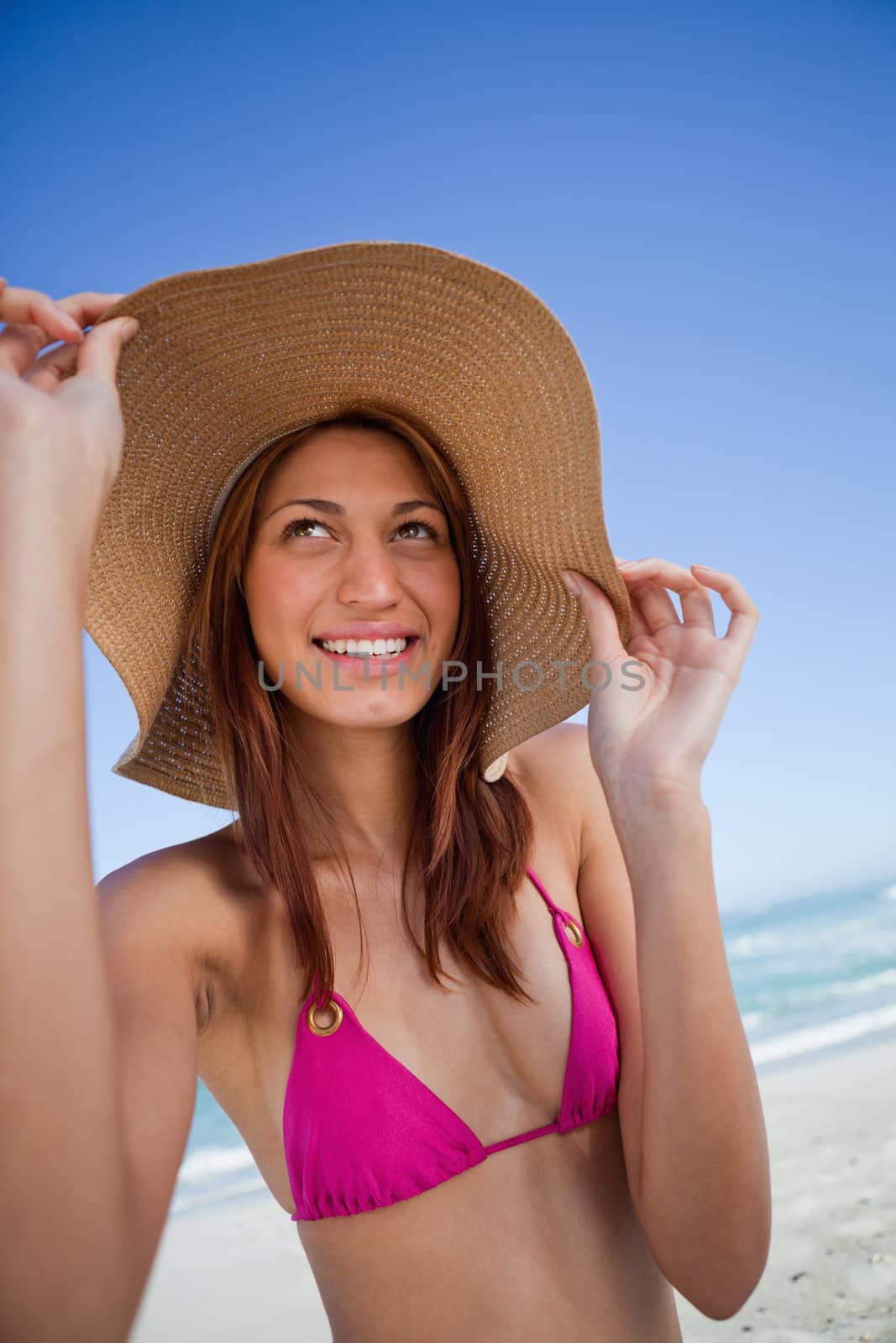 Smiling attractive teenager holding her hat brim while standing on the beach