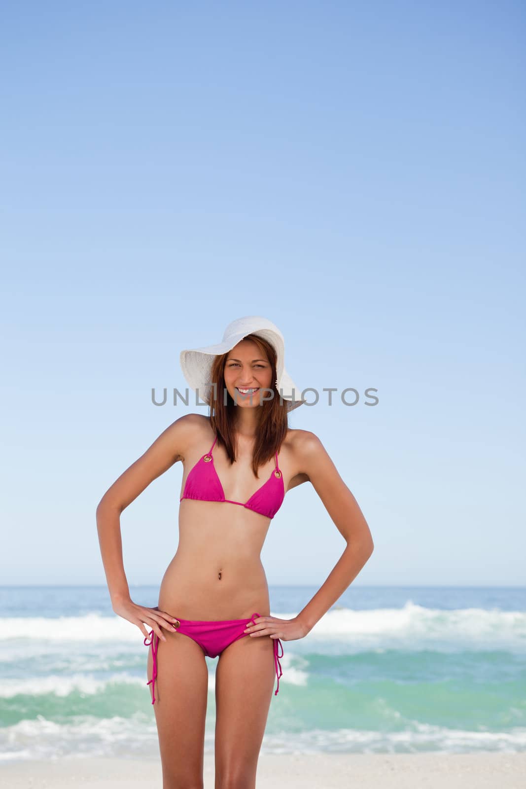 Smiling young attractive woman placing hands on hips while standing on the beach