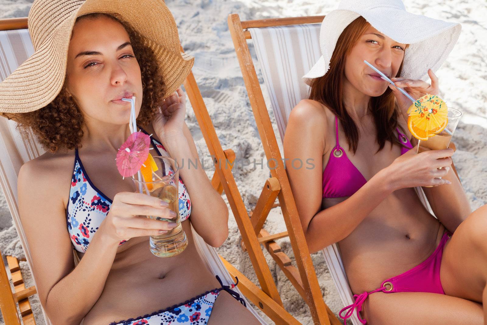 Young attractive women sipping their exotic cocktails while sitting on deck chairs