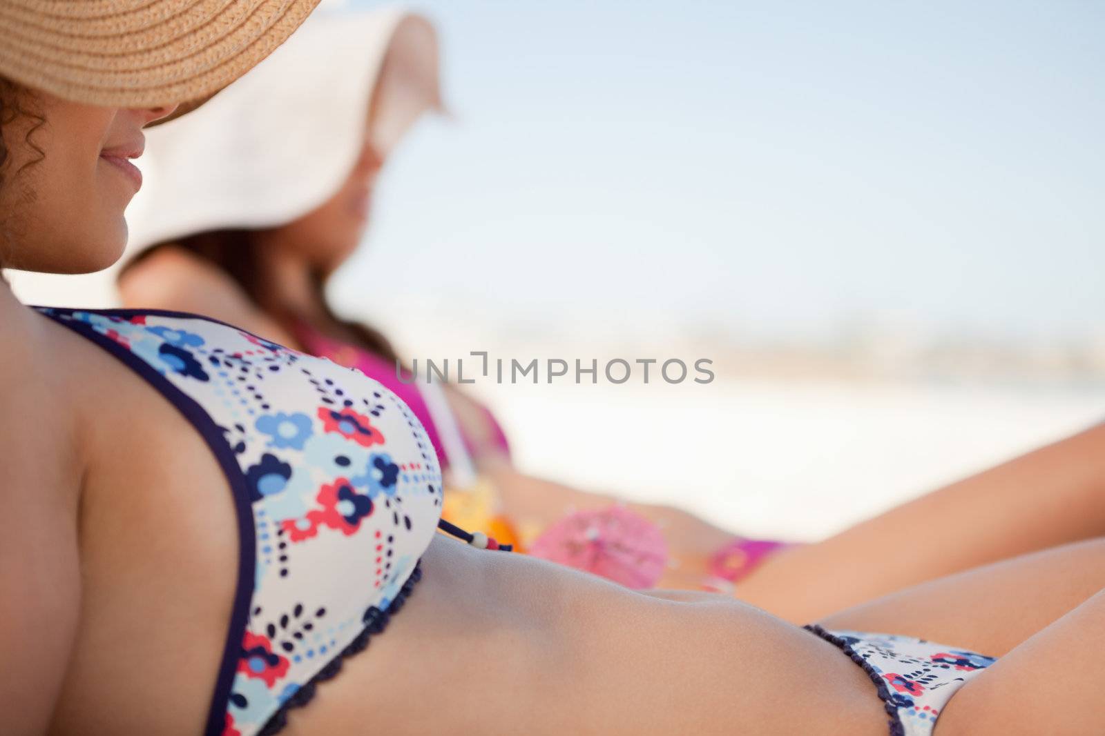 Attractive young woman in bikini lying on the beach with her friend beside her