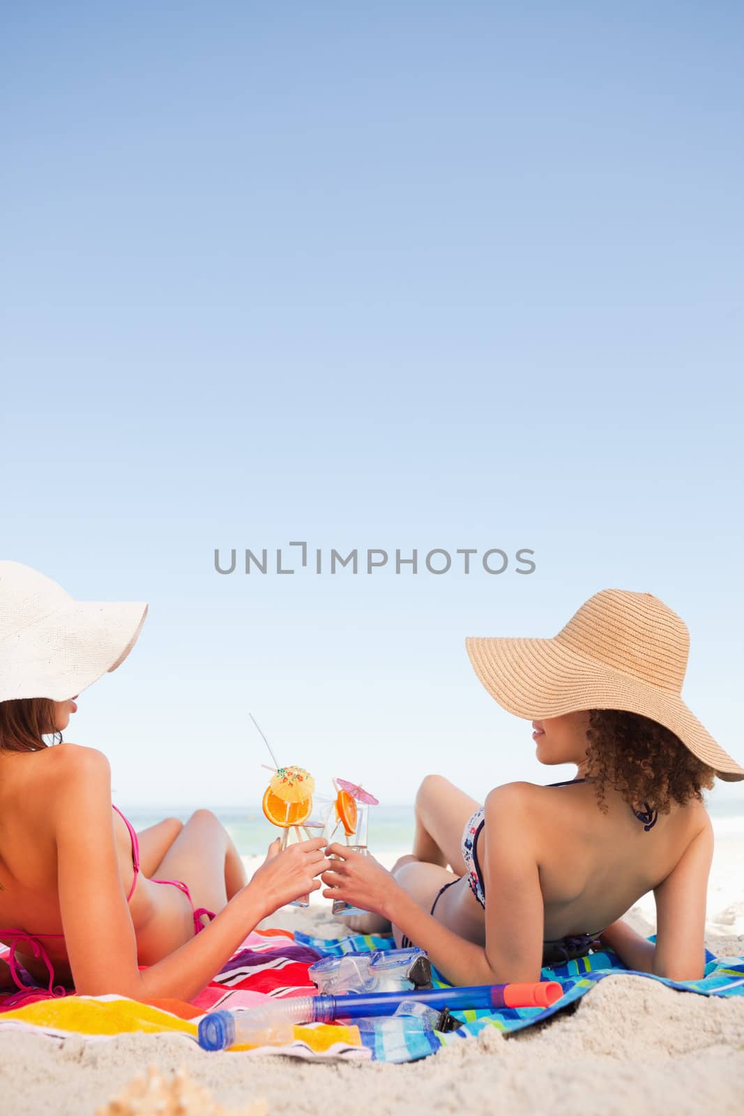 Young women on beach towels clinking their glasses while looking at each other