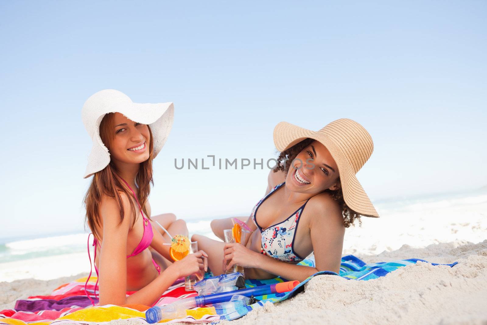 Young smiling women lying on beach towels while looking at the c by Wavebreakmedia