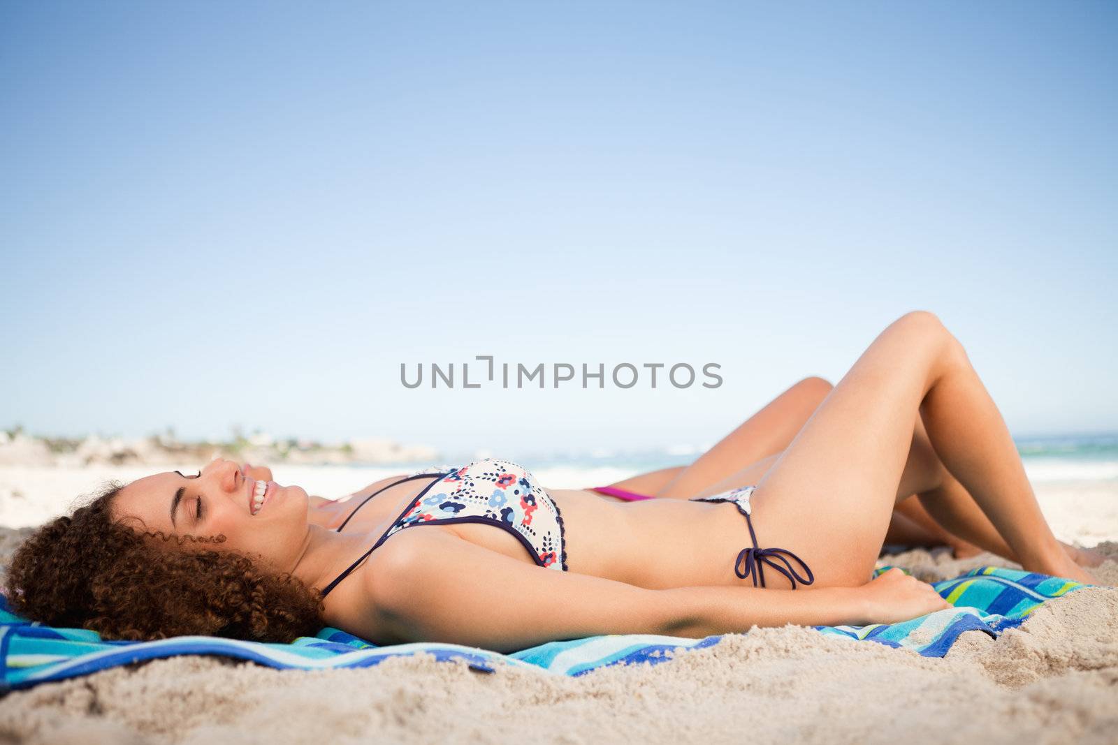 Young smiling woman lying on her beach towel and accompanied by her friend