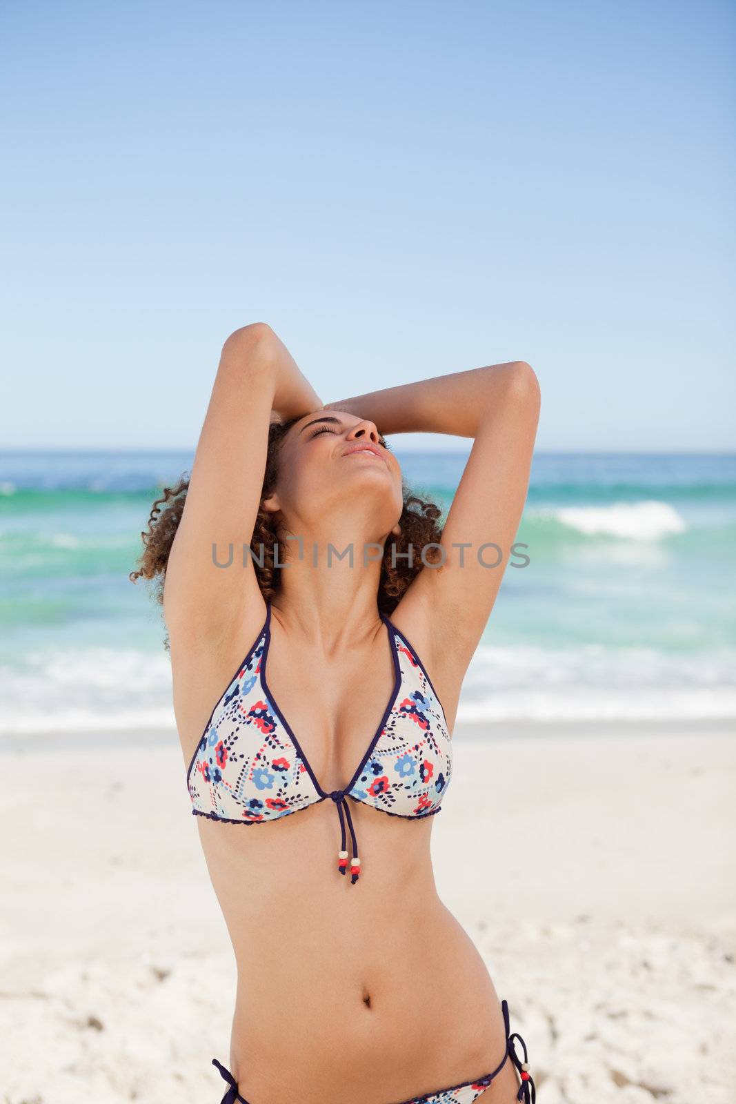 Young woman in bikini raising her arms and looking up by Wavebreakmedia