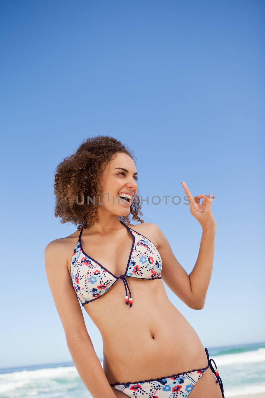 Young woman standing on the beach while pointing her finger up with a smile