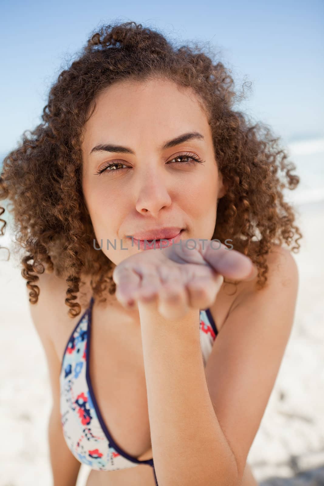 Young woman blowing a kiss while staring at the camera and standing on the beach