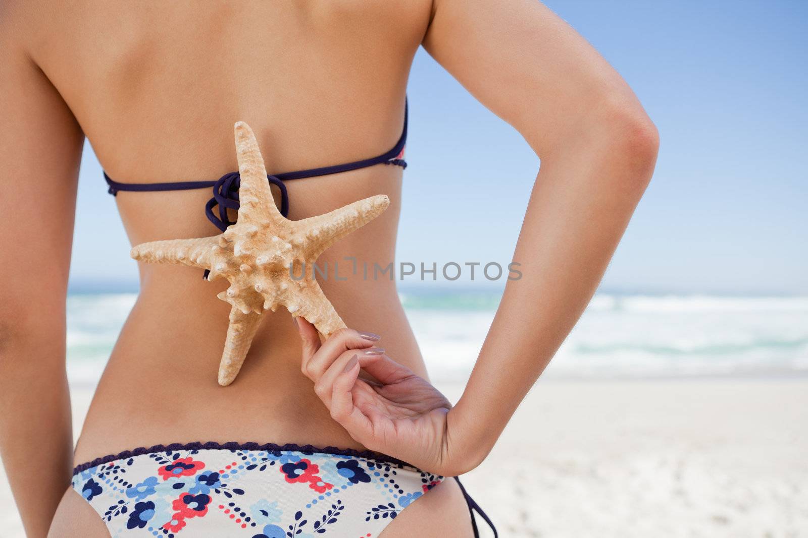 Young woman holding a starfish on her back with one hand by Wavebreakmedia