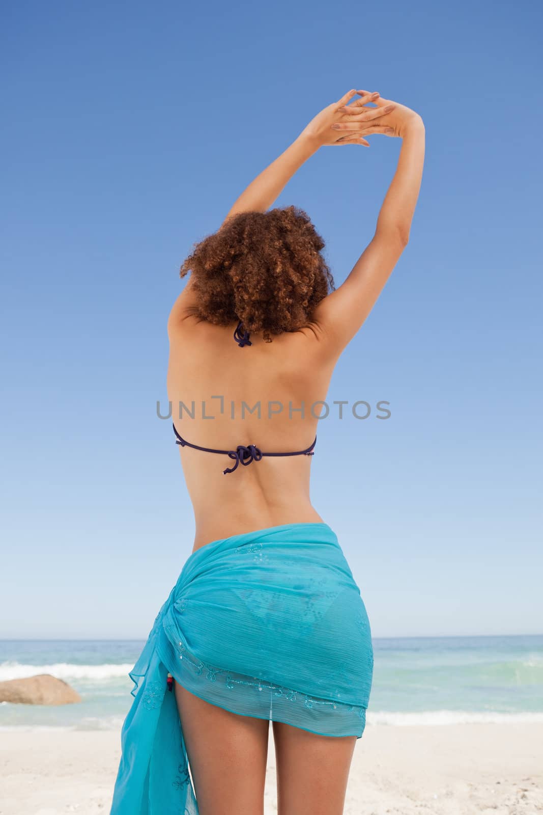 Rear view of a beautiful woman in beachwear raising and crossing her hands