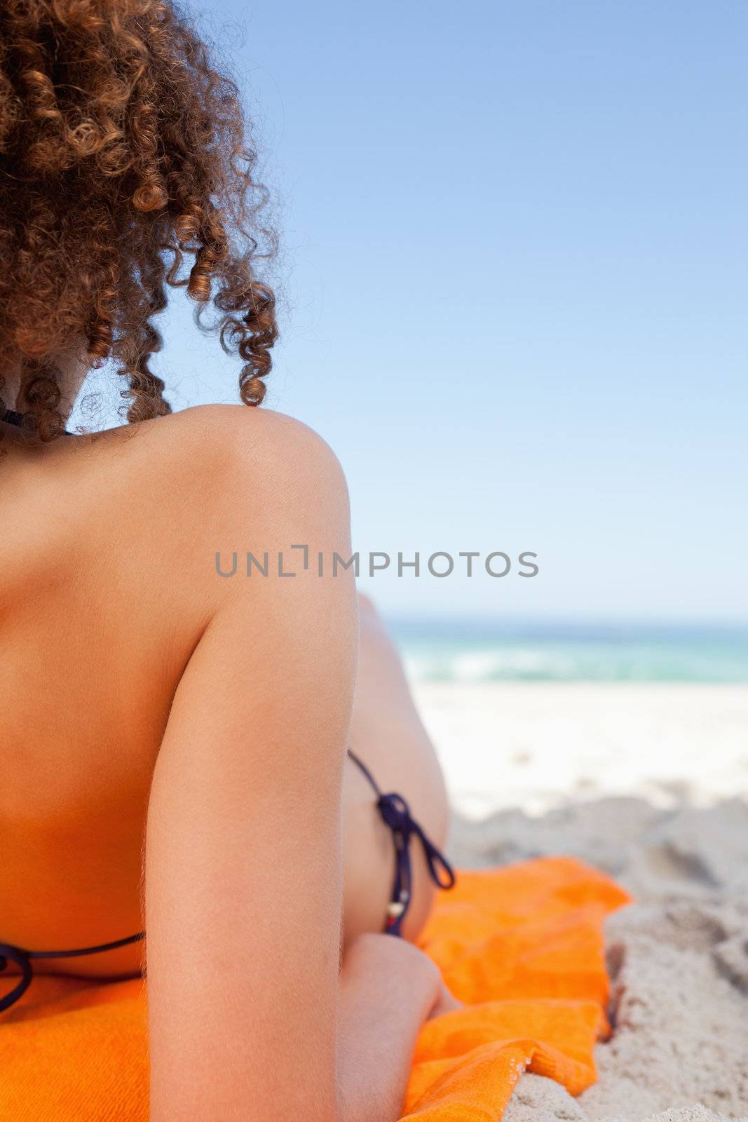 Back view of a young woman lying on her orange beach towel by Wavebreakmedia