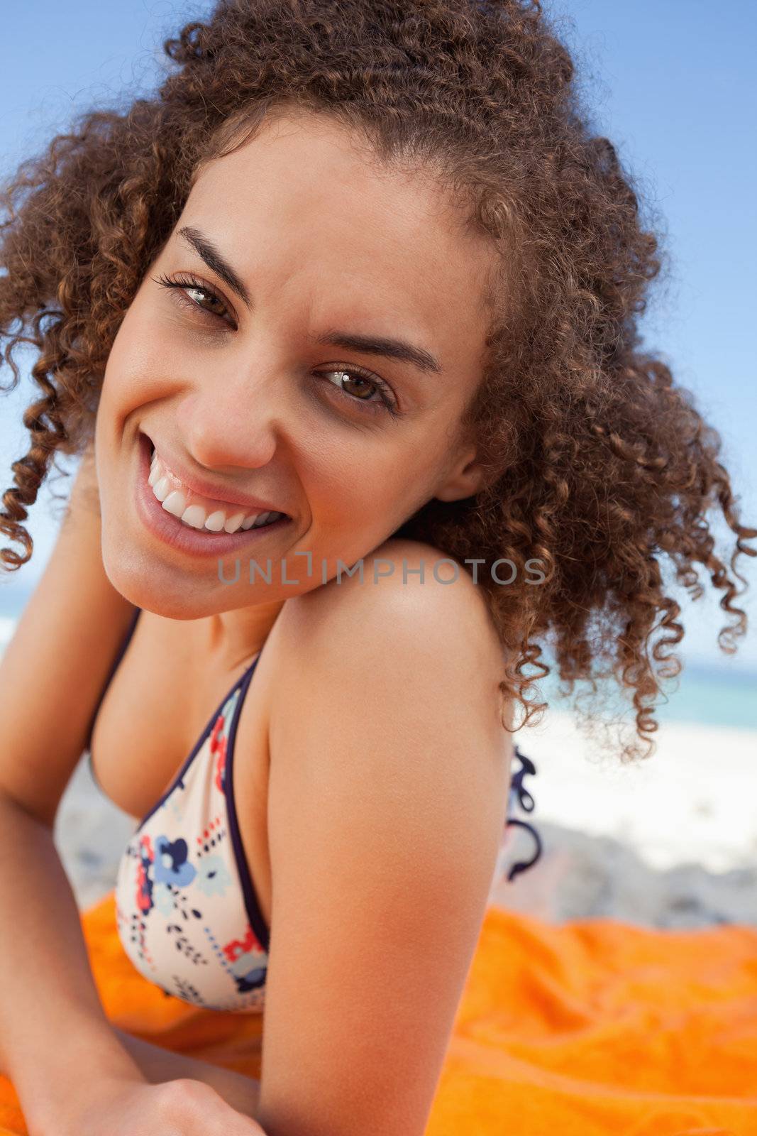 Young smiling woman lying down on a beach towel while staring at by Wavebreakmedia