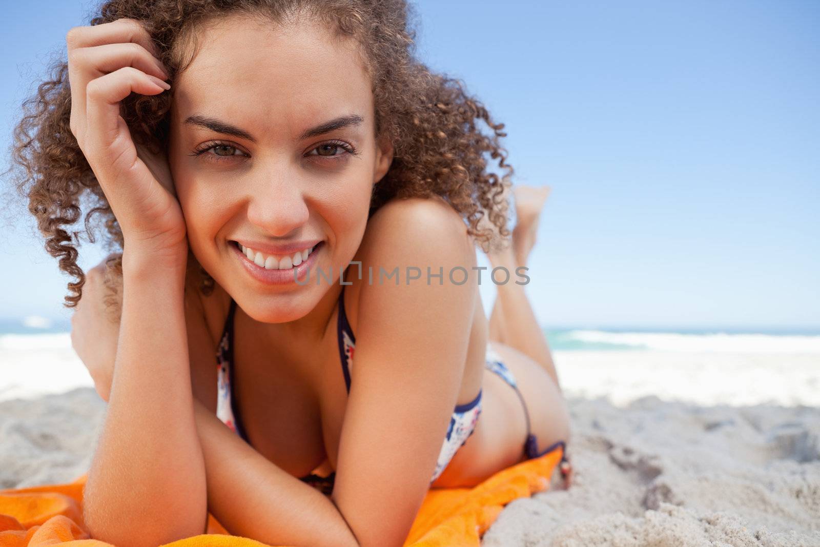 Young woman lying down while showing a great smile with her hand by Wavebreakmedia