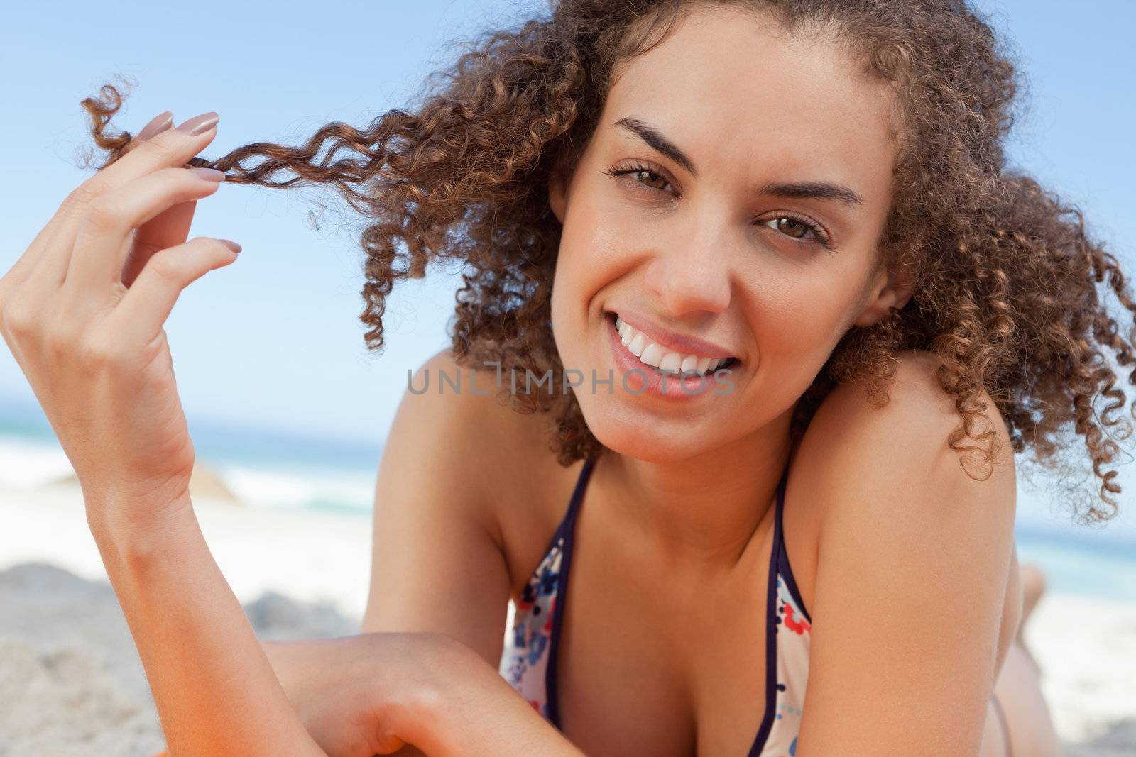 Smiling young woman holding a lock of hair with her fingers by Wavebreakmedia
