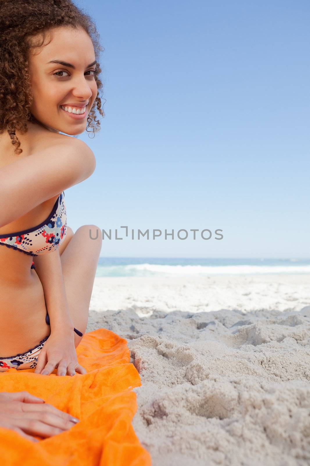 Young smiling woman turning her head back while sitting in front of the sea