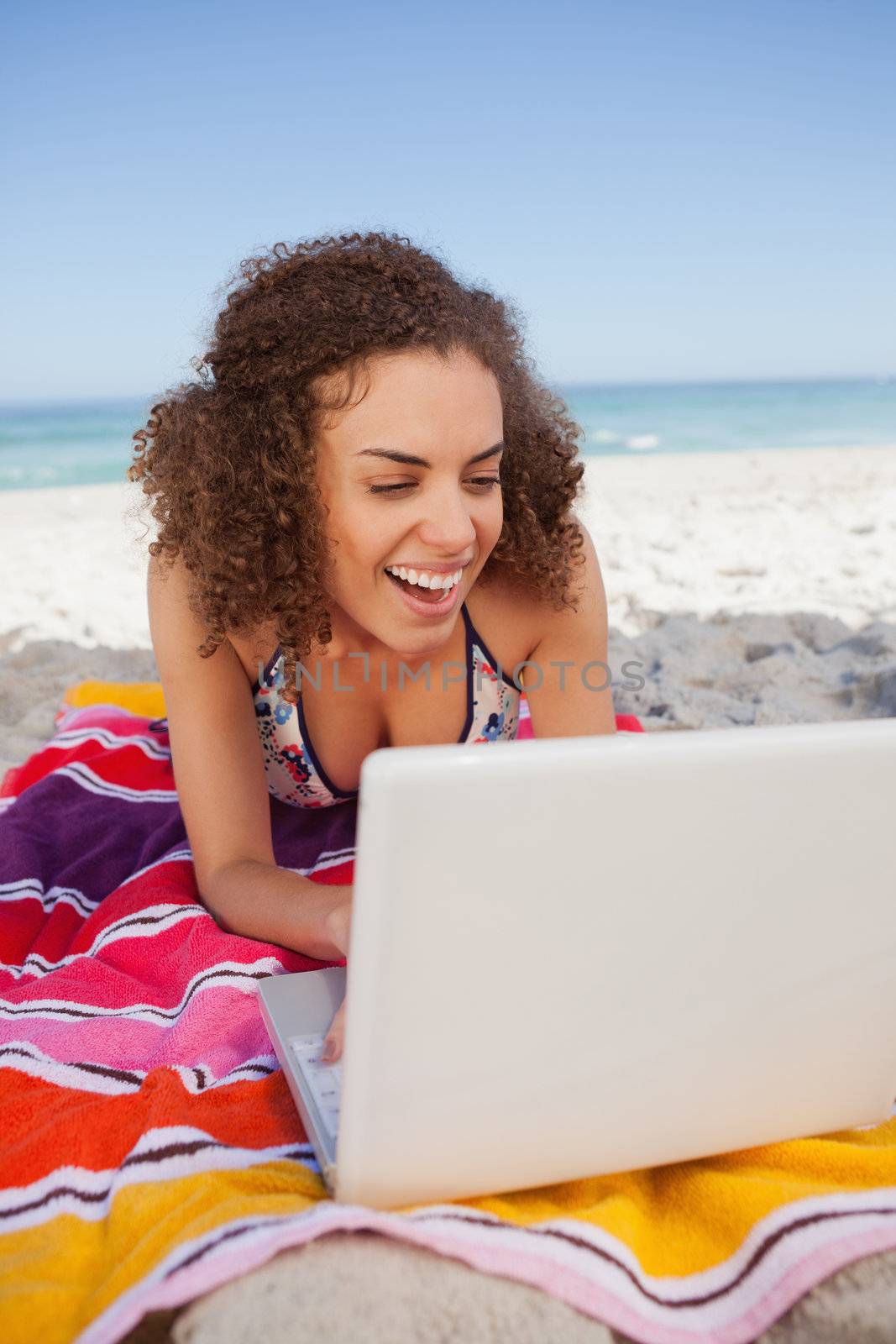 Young attractive woman using a laptop on the beach while laughin by Wavebreakmedia