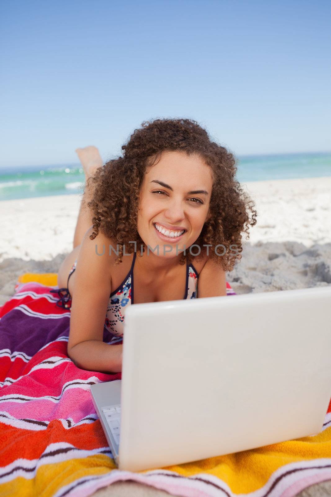 Young smiling woman typing on her laptop while lying on the beac by Wavebreakmedia