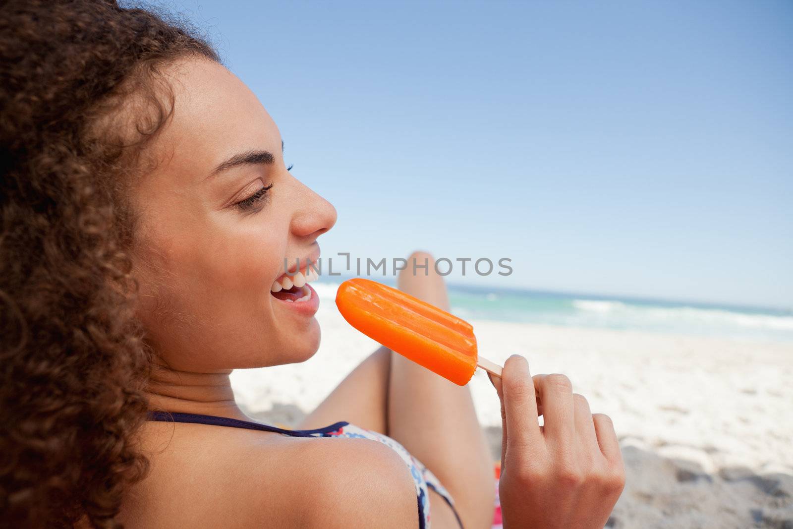 Young smiling woman holding a popsicle while lying on the beach
