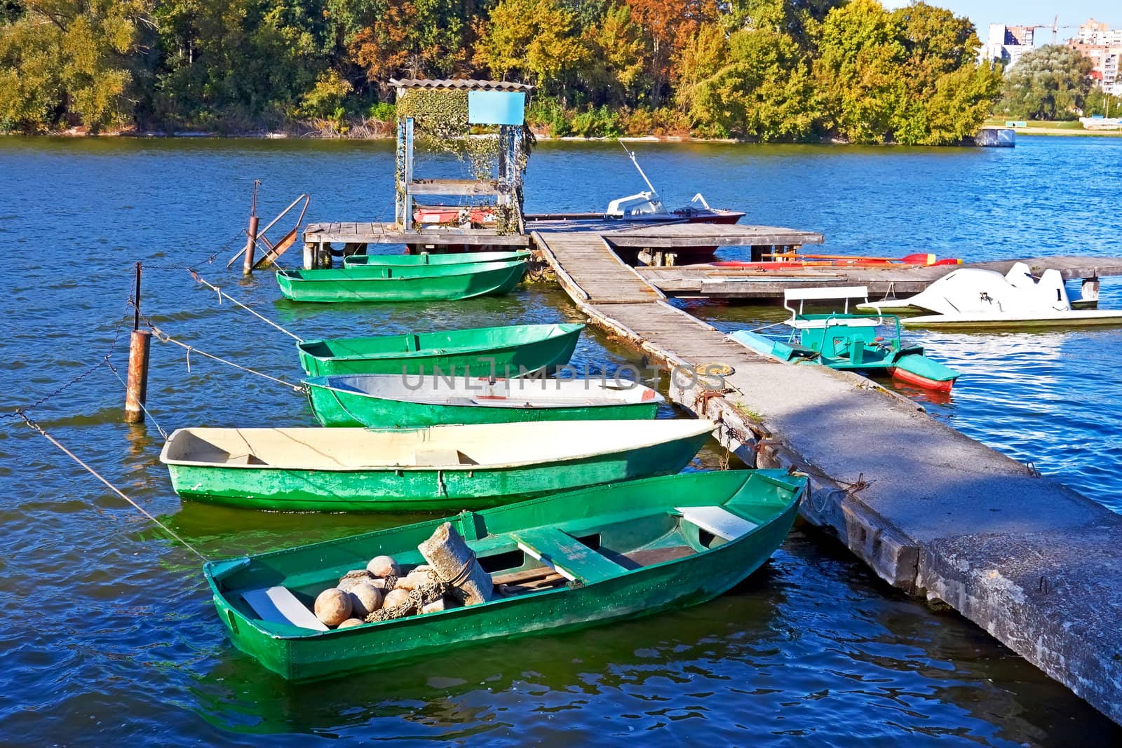 Group of small fishing boats and other craft are tied near the old pier. Fine autumn day. Southern Bug River in Khmelnytsky, Ukraine