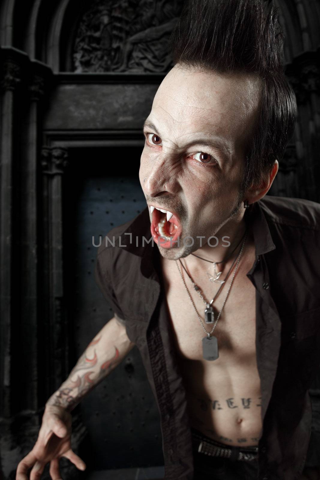 Photo of a male vampire with mouth open and fangs showing.  Harsh lighting and heavily filtered for scarier feel.