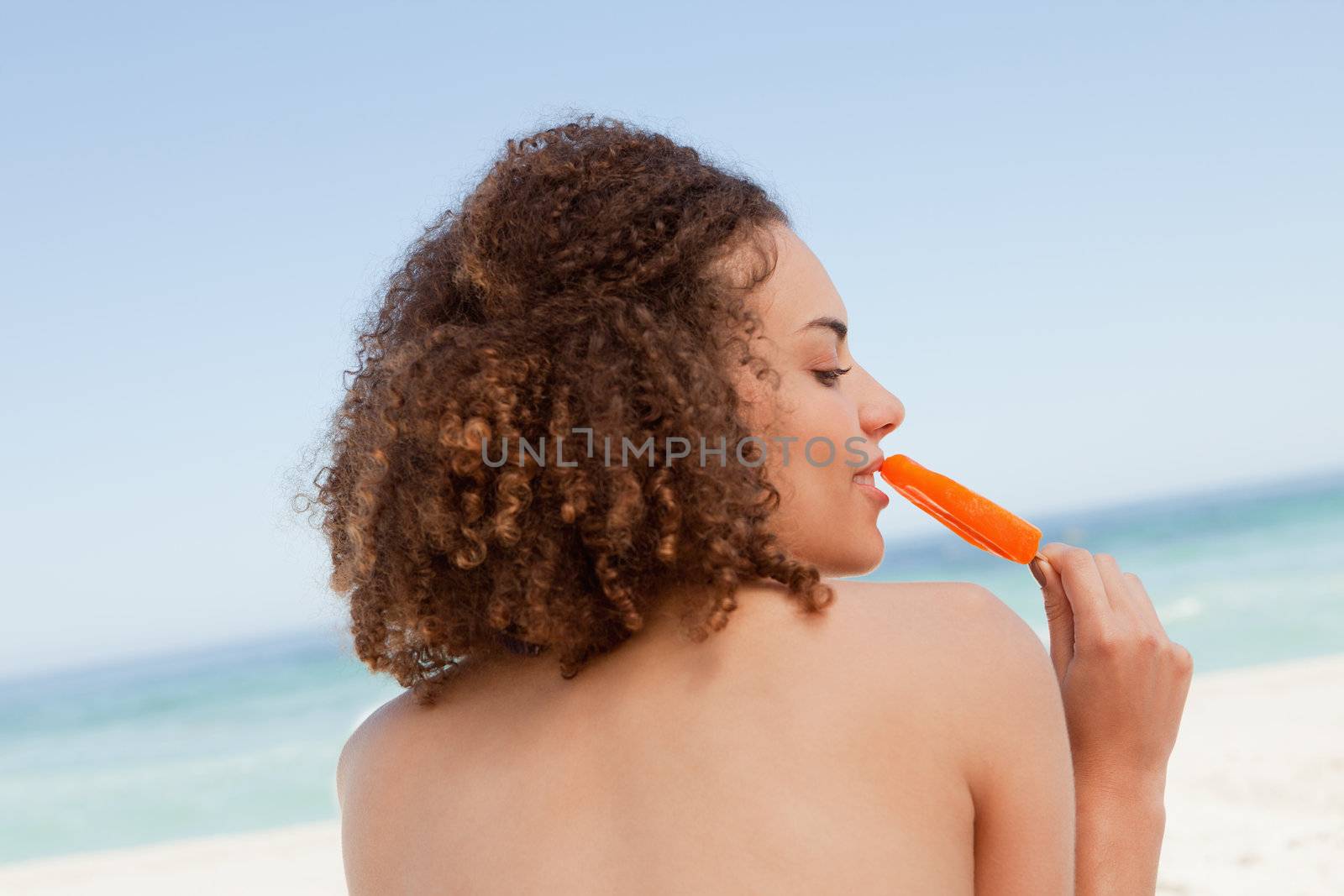 Attractive young brunette eating an orange ice lolly in front of by Wavebreakmedia
