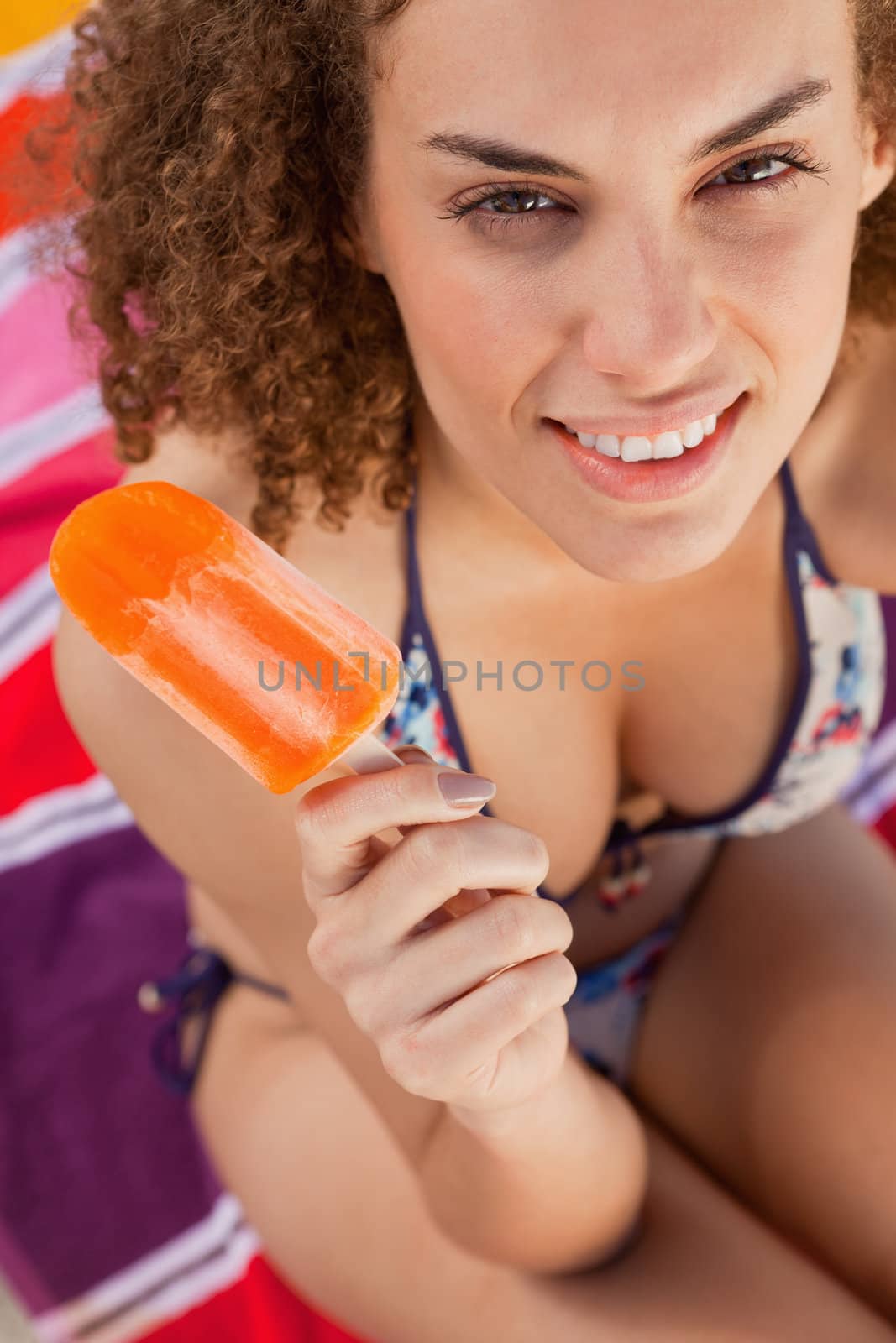 Young attractive woman in bikini holding an ice lolly while looking at the camera by Wavebreakmedia