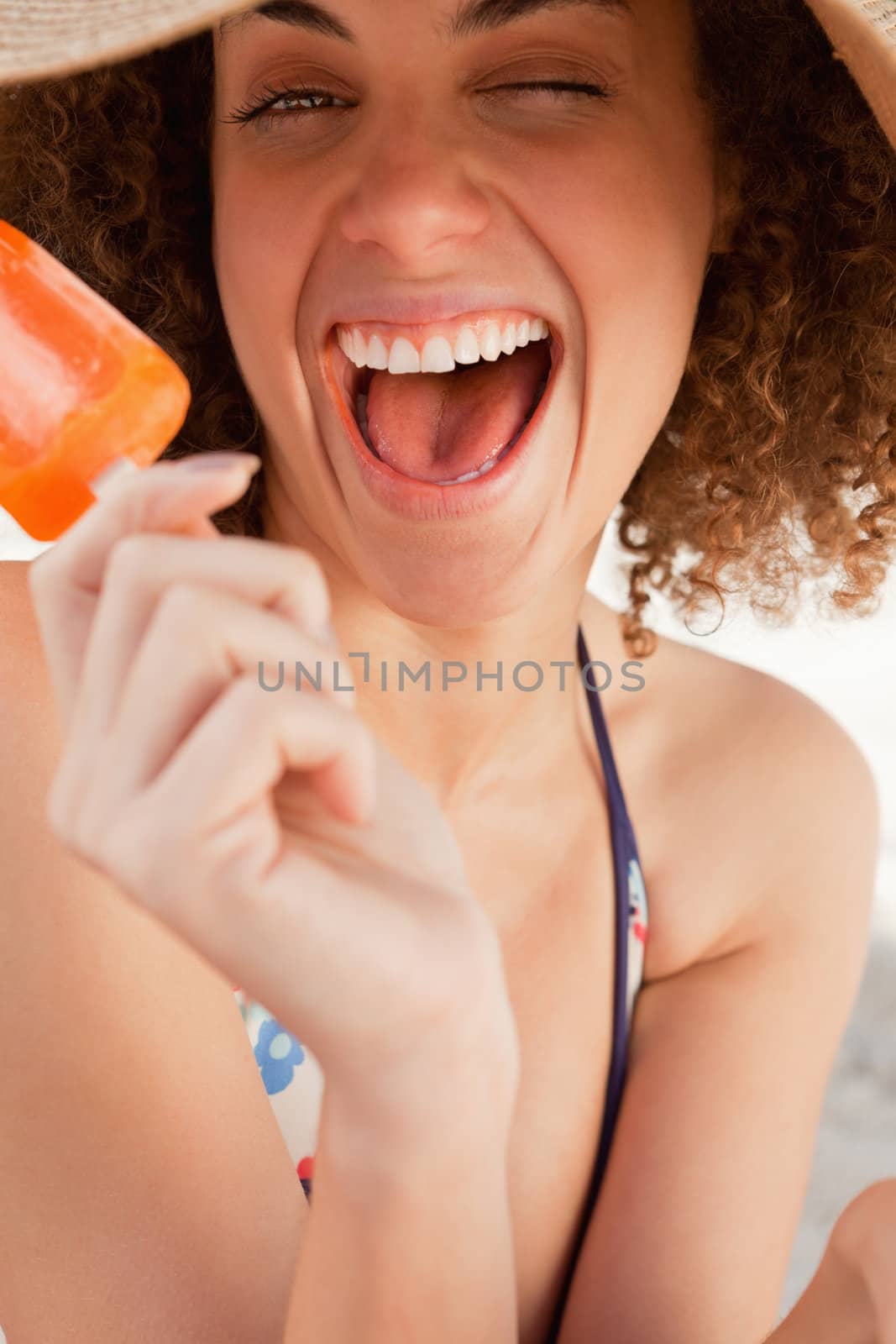 Young woman sitting on the beach while laughing and holding an ice cream by Wavebreakmedia