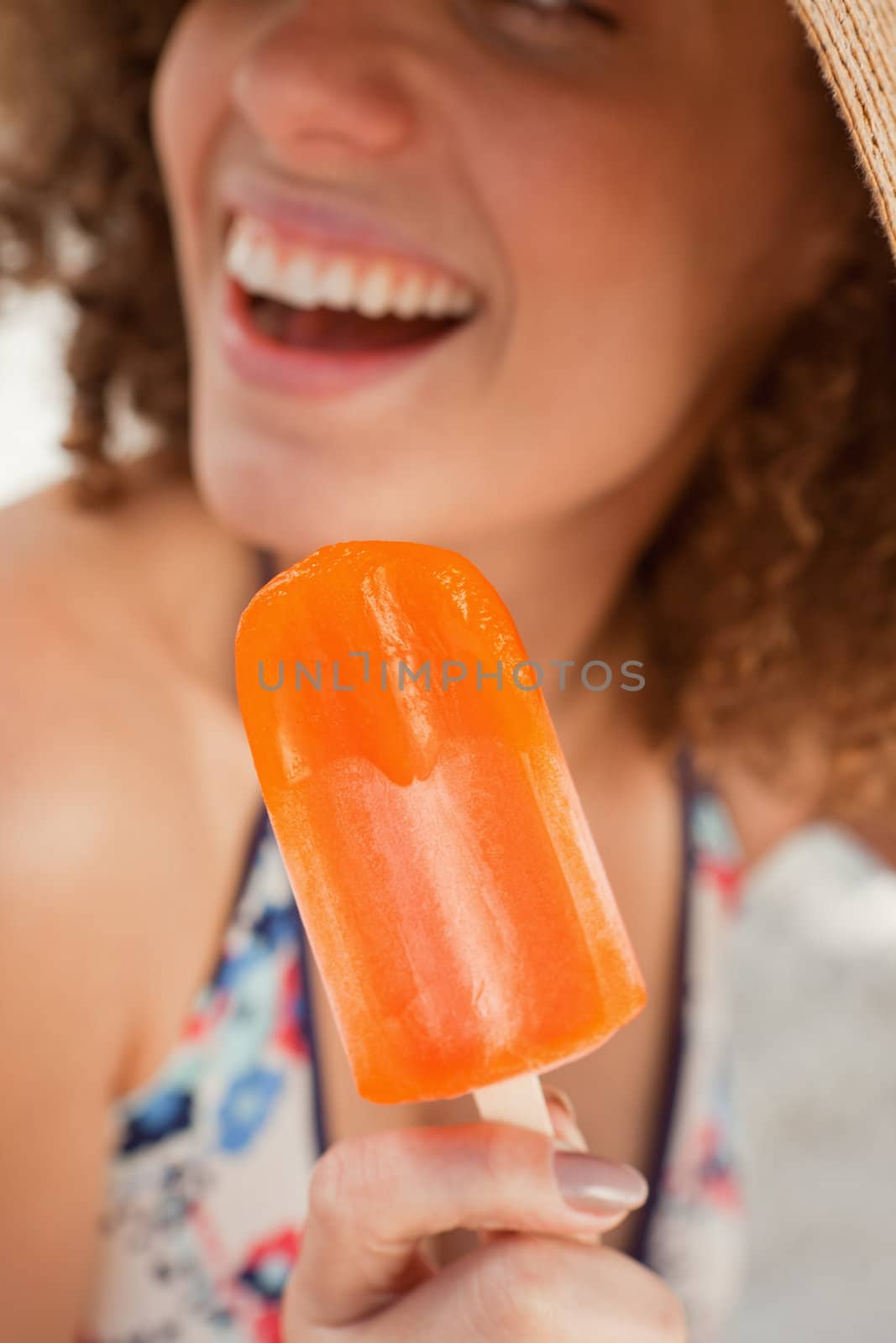 Orange popsicle held by a smiling young woman by Wavebreakmedia