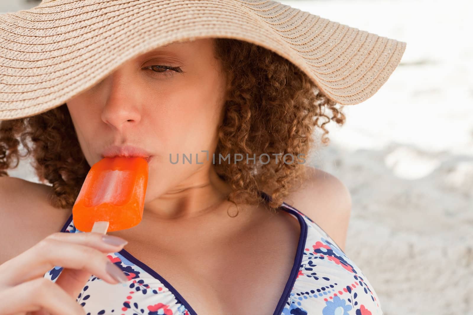 Relaxed young woman wearing a straw hat while eating an ice lolly by Wavebreakmedia