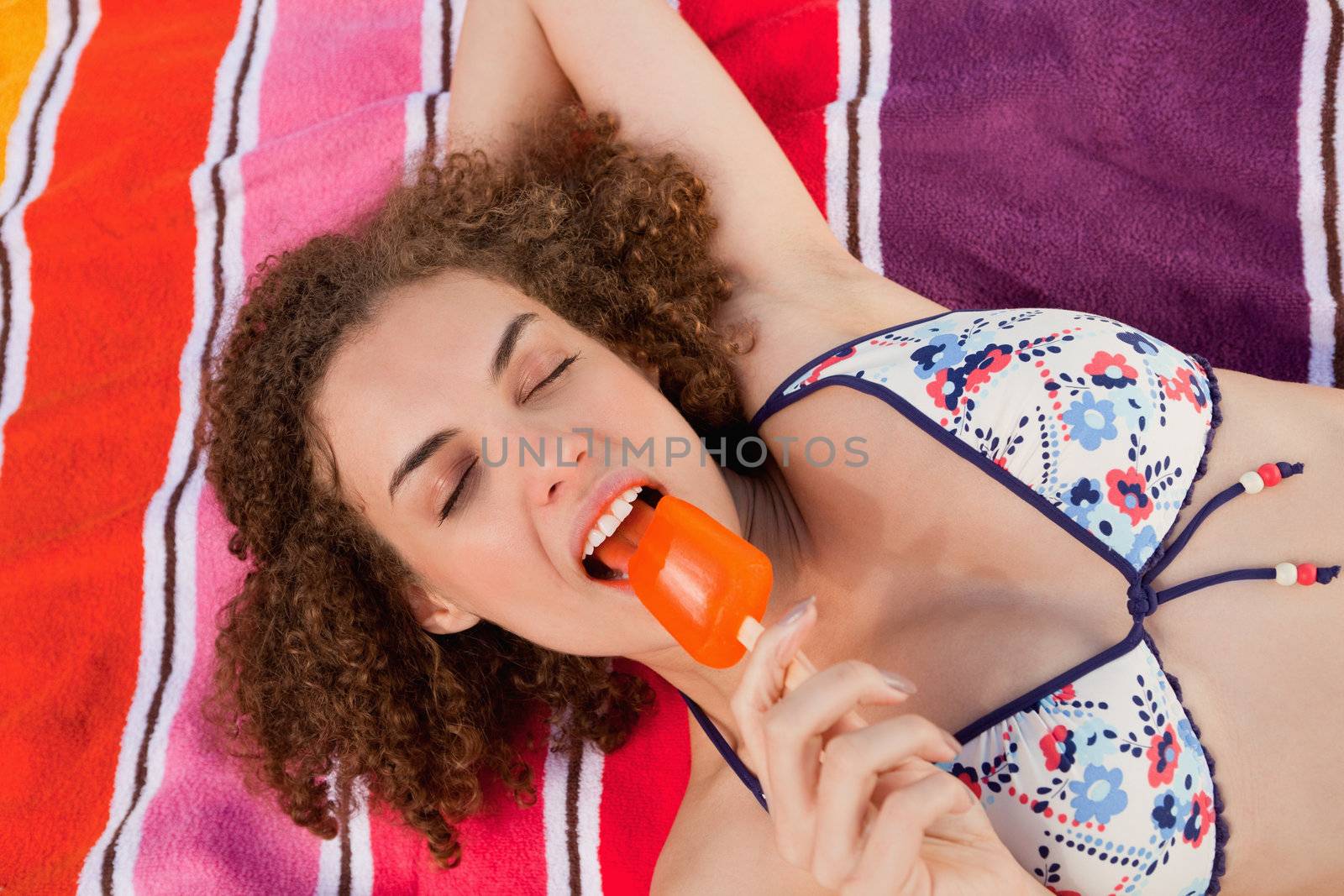 Young beautiful woman looking relaxed while eating a delicious orange ice lolly