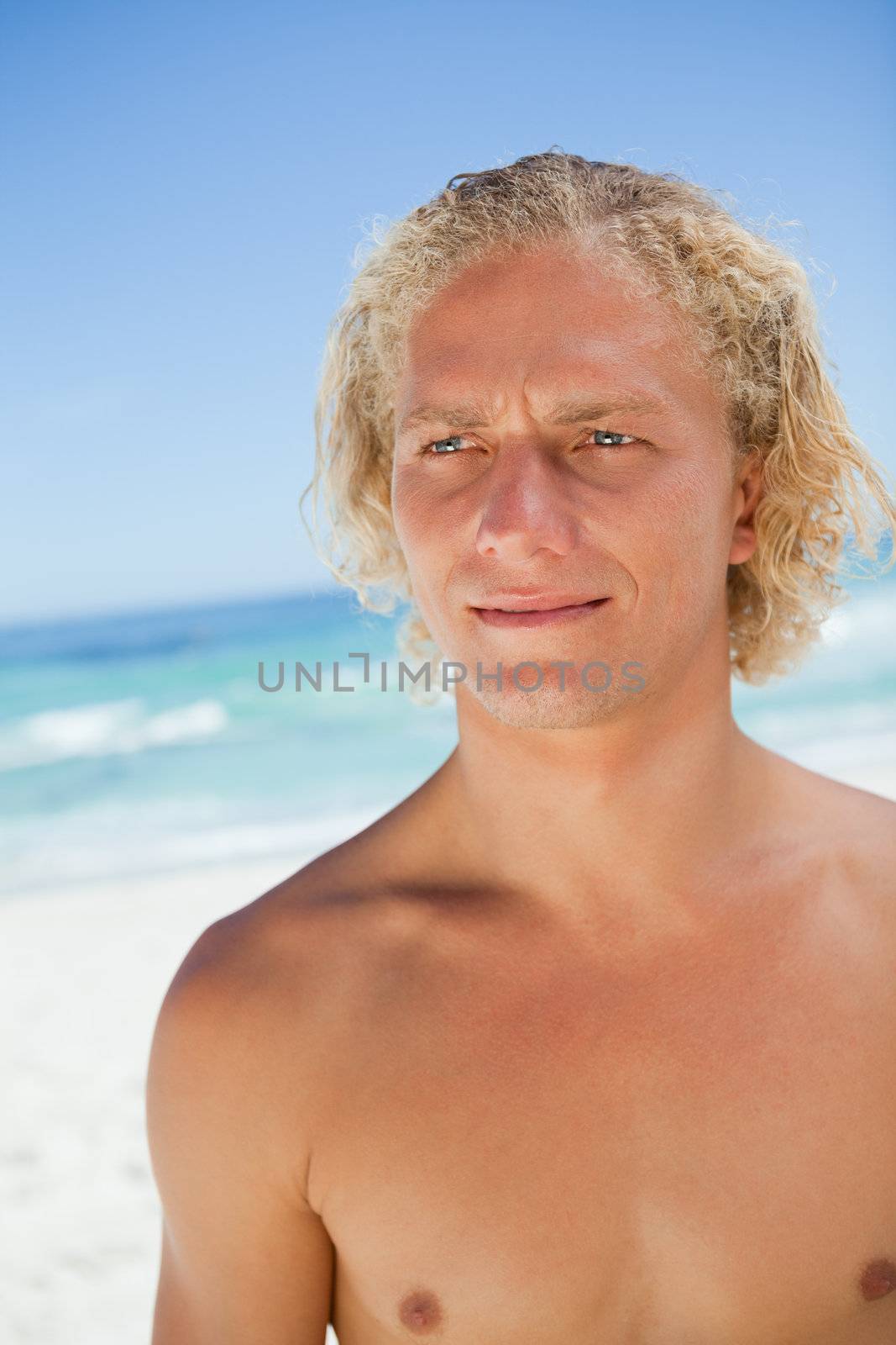 Serious blonde man looking towards the side while standing on the beach by Wavebreakmedia