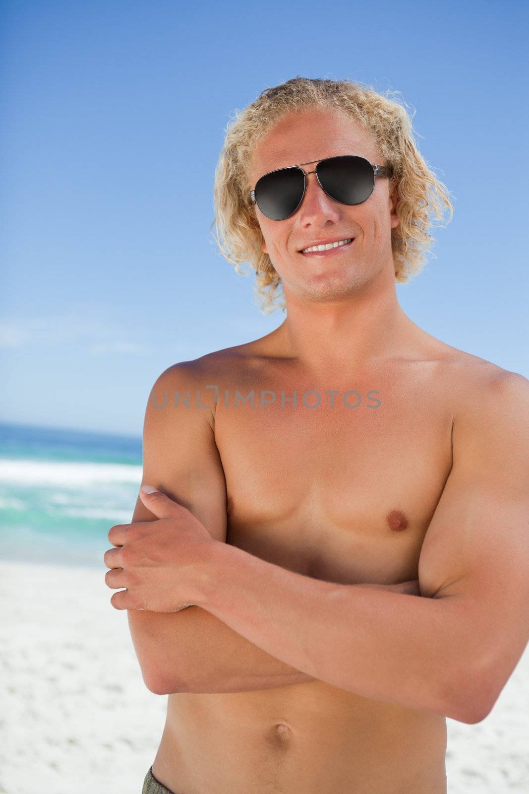 Young attractive man crossing his arms while standing in swimsuit on the beach