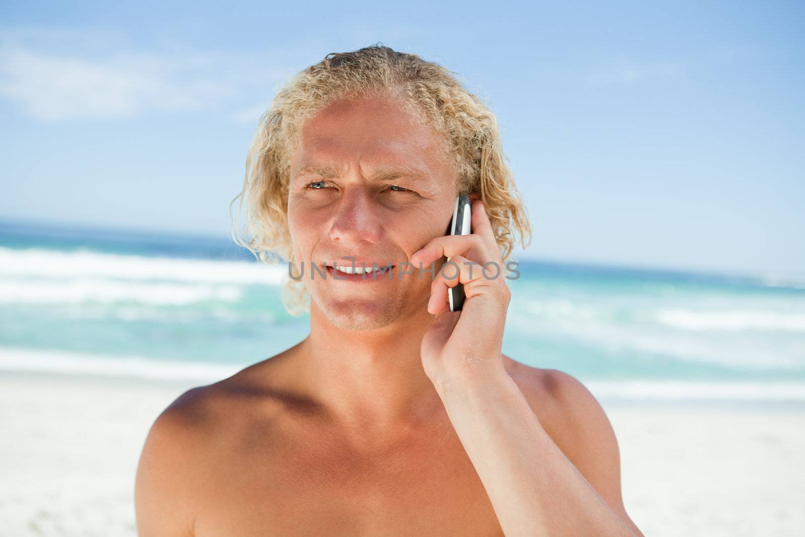 Blonde man standing in front of the ocean while using his cellphone