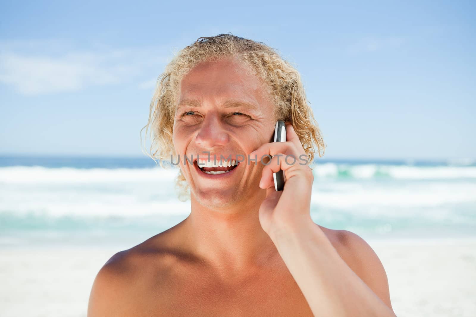 Smiling man using his mobile phone while standing on the beach by Wavebreakmedia