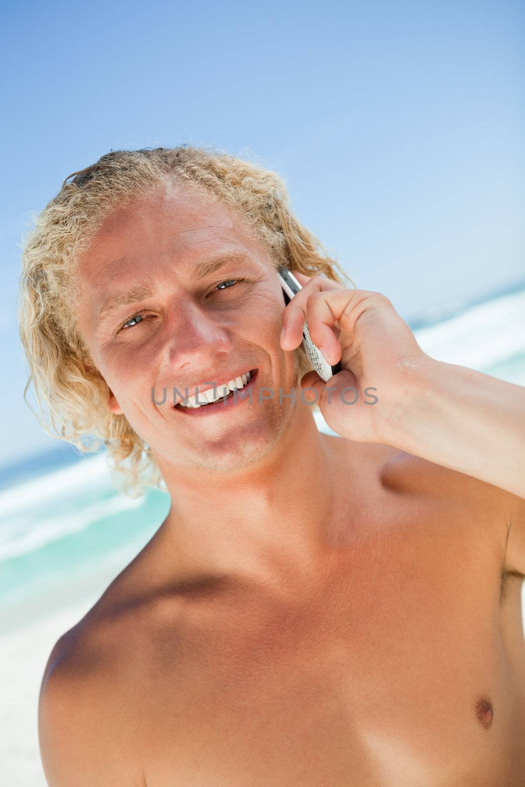Smiling blonde man looking at the camera while calling with his cellphone by Wavebreakmedia