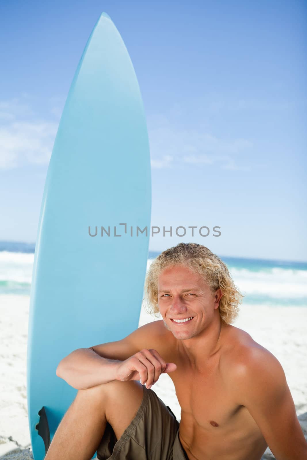 Smiling man sitting on the beach with his arm on his leg  by Wavebreakmedia