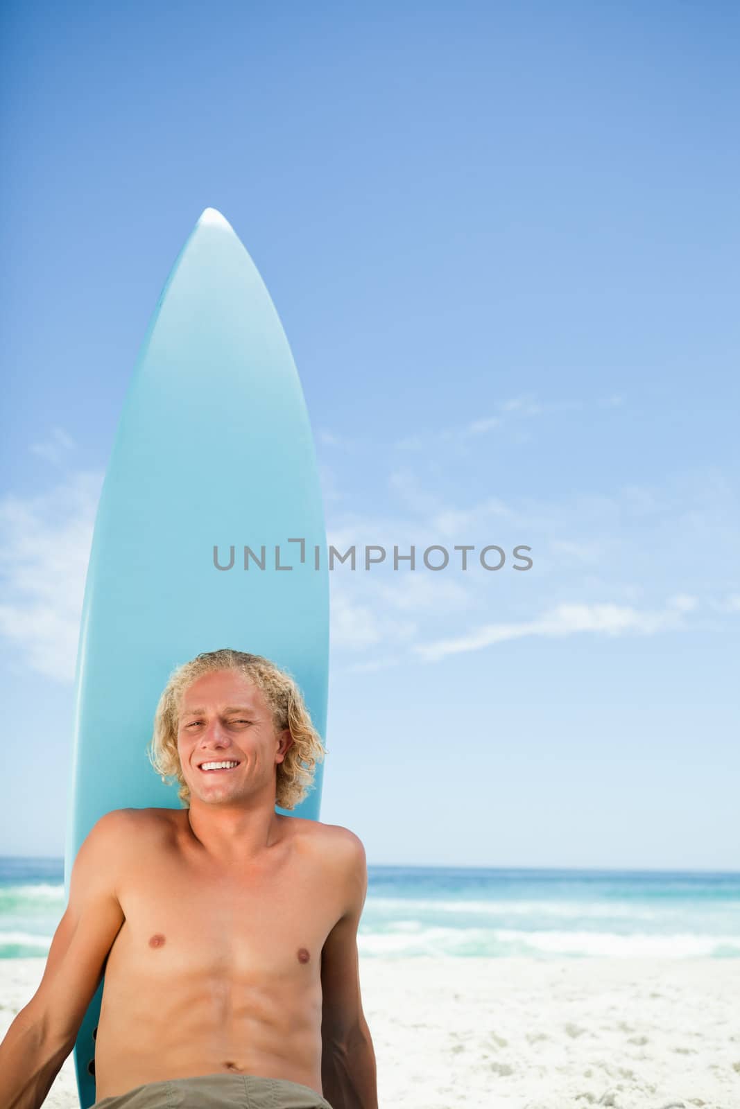 Smiling blonde man sunbathing on the beach with his surfboard next to him by Wavebreakmedia