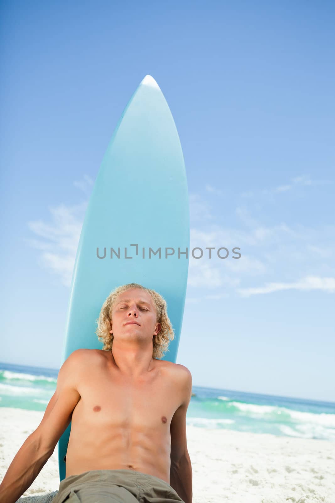 Young relaxed man sitting on the beach while sunbathing and closing his eyes