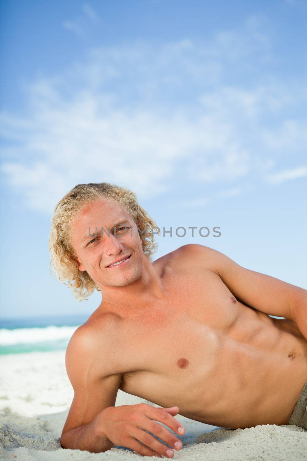 Young man lying on the beach while looking at the camera and showing a great smile