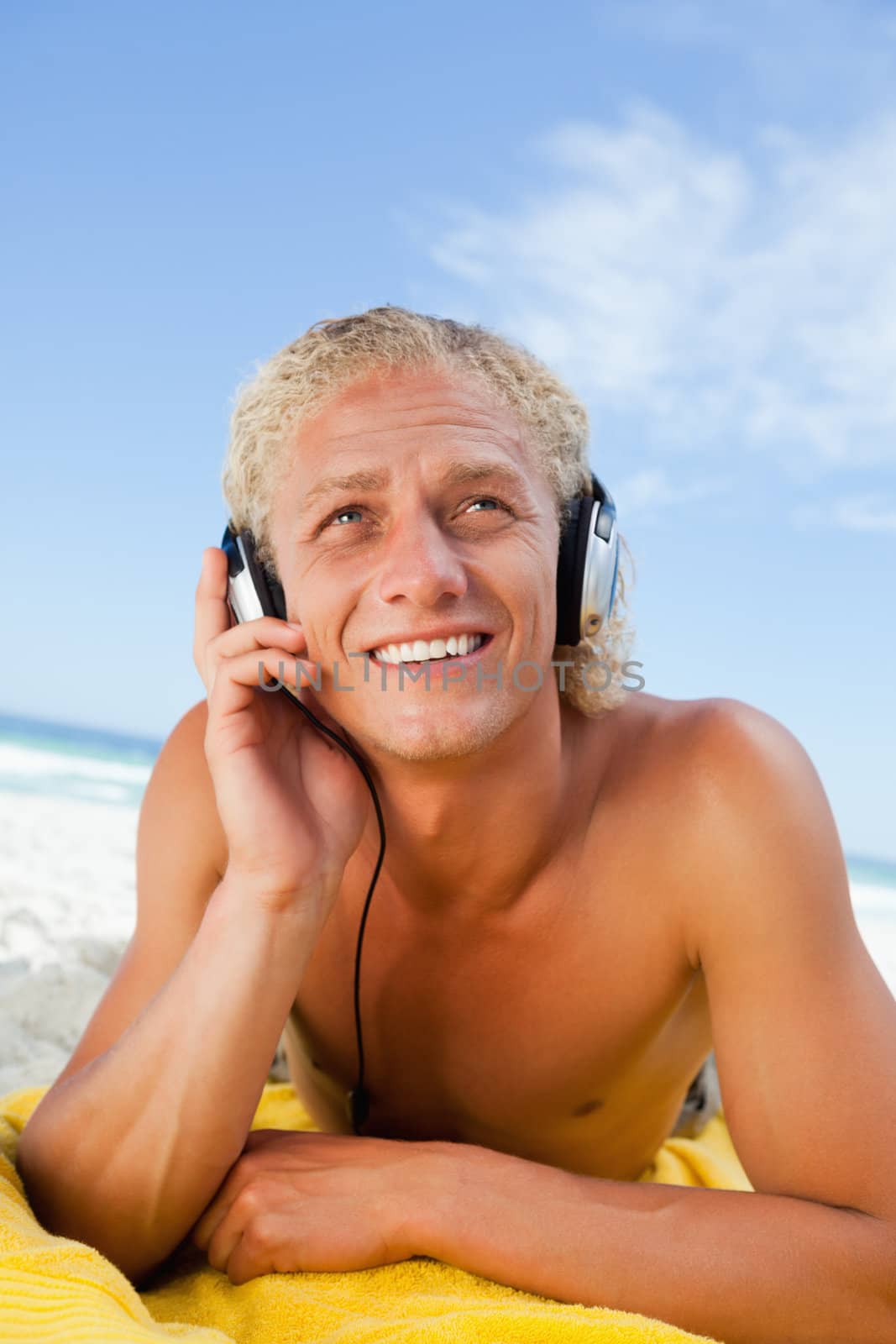 Smiling man lying on the beach while listening to music by Wavebreakmedia