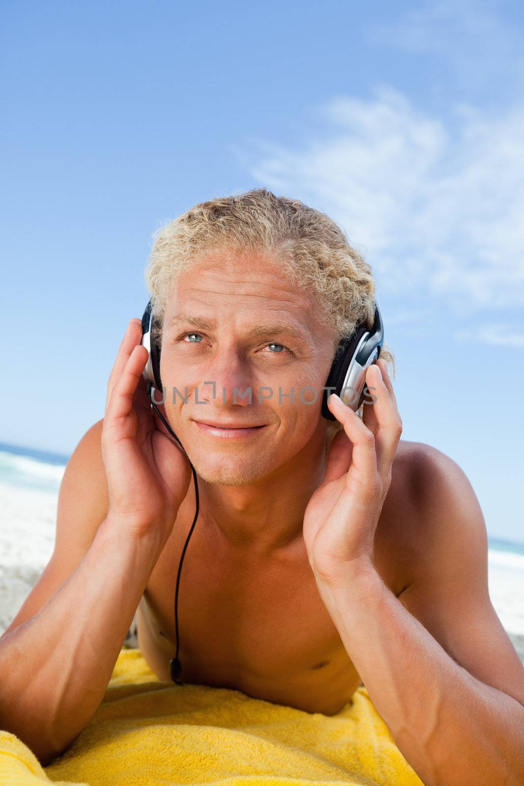 Smiling young man lying on his yellow beach towel while listening to music by Wavebreakmedia