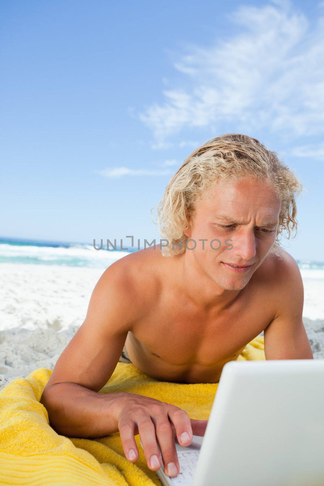 Blonde man lying on the beach while using his laptop in a very concentrated way by Wavebreakmedia