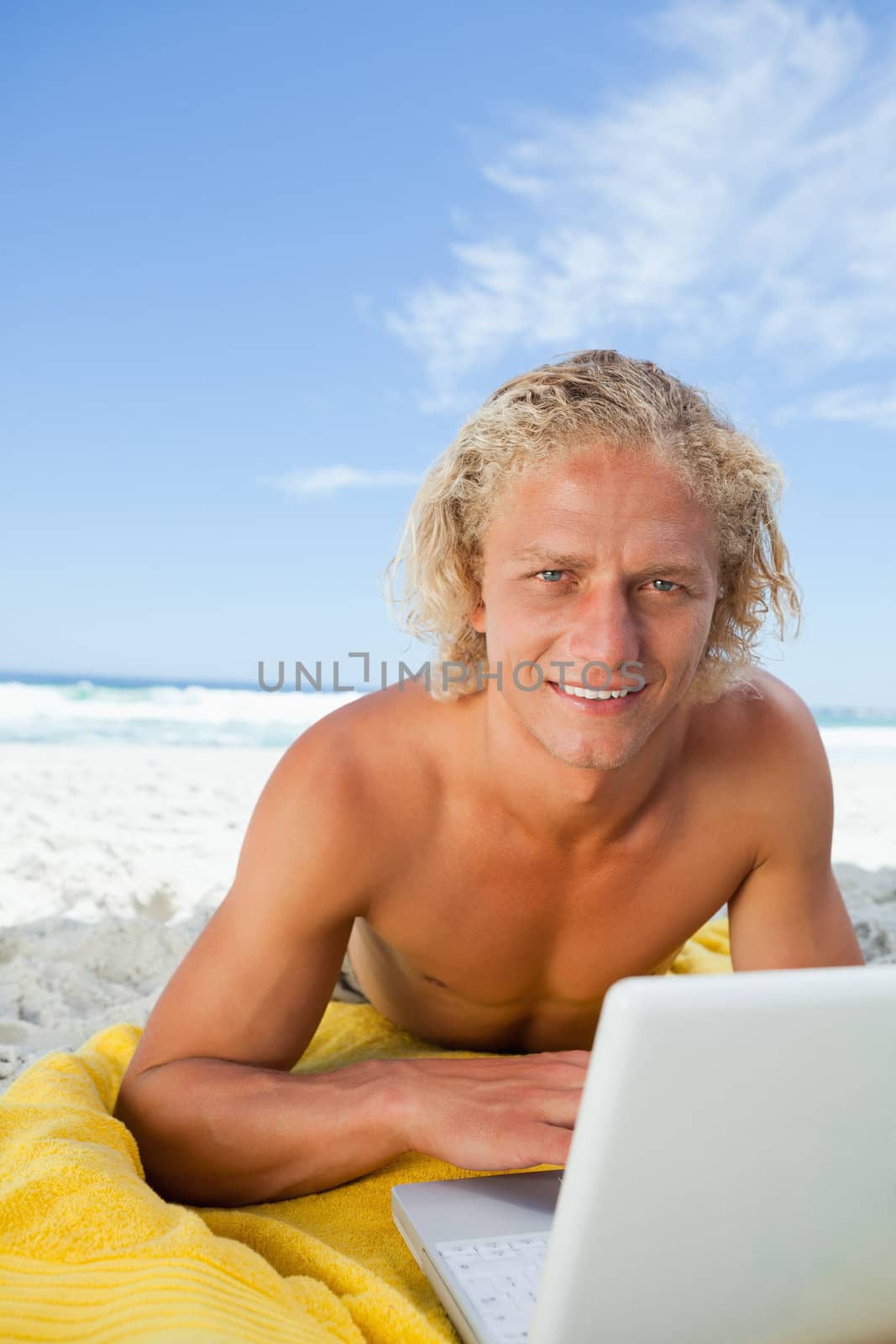 Smiling blonde man looking at the camera while using his laptop by Wavebreakmedia
